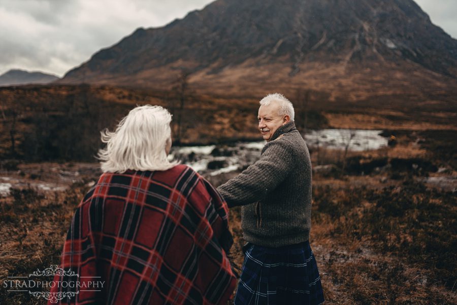 beautiful scenery, deers, elderly couple, engagement photography, glasgow photographer, glen etive, Glencoe, grandma, grandpa, hiking, kilt, landscapes, man and woman, marr, marriage, old couple, old married couple, older couple photo shoot in Glencoe Scotland, outlander, poncho, posing ideas, scotland, scottish couple, scottish highlands, senior couple, tartan