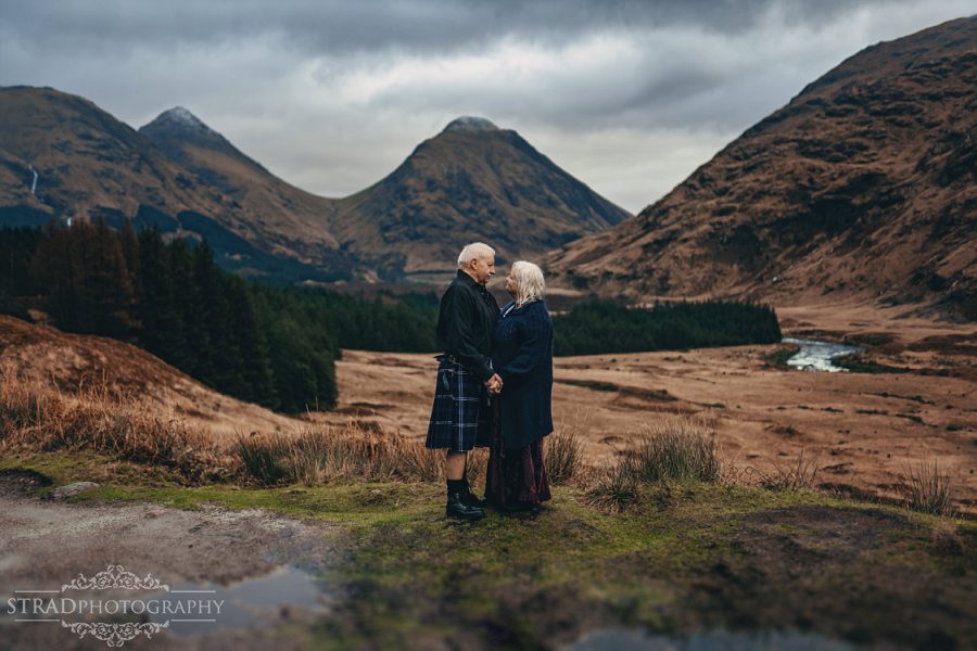 beautiful scenery, deers, elderly couple, engagement photography, glasgow photographer, glen etive, Glencoe, grandma, grandpa, hiking, kilt, landscapes, man and woman, marr, marriage, old couple, old married couple, older couple photo shoot in Glencoe Scotland, outlander, poncho, posing ideas, scotland, scottish couple, scottish highlands, senior couple, tartan