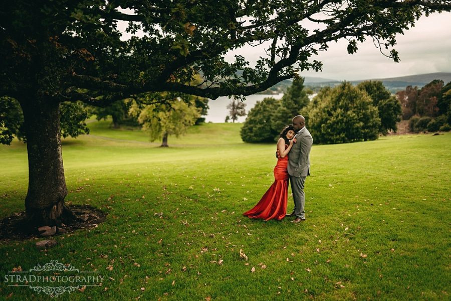 Bride in the red dress and the groom standing together under the tree in the park