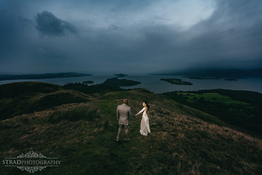 Wide angle dramatic photo of the bride and groom on the top of Conic Hill