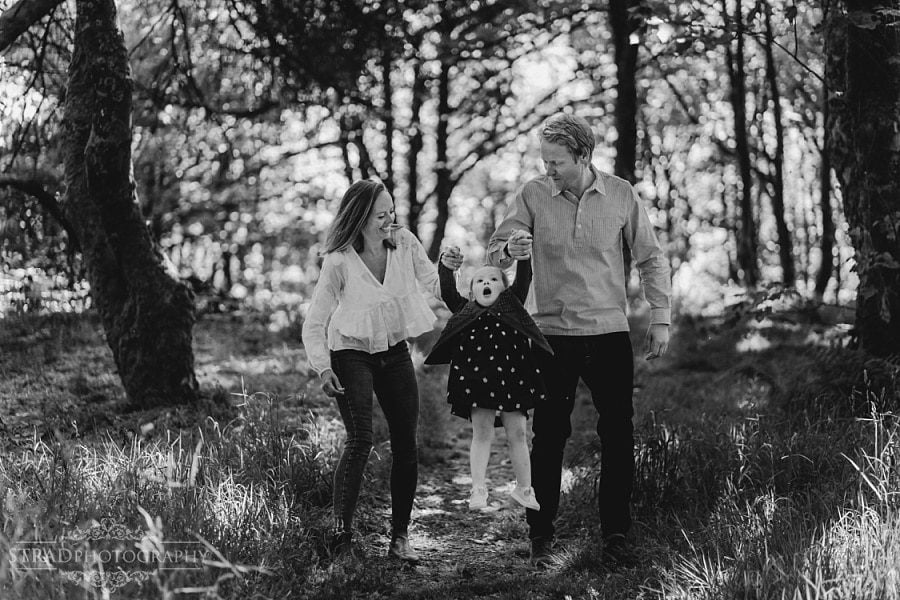 Parents swing their daughter in the wood.