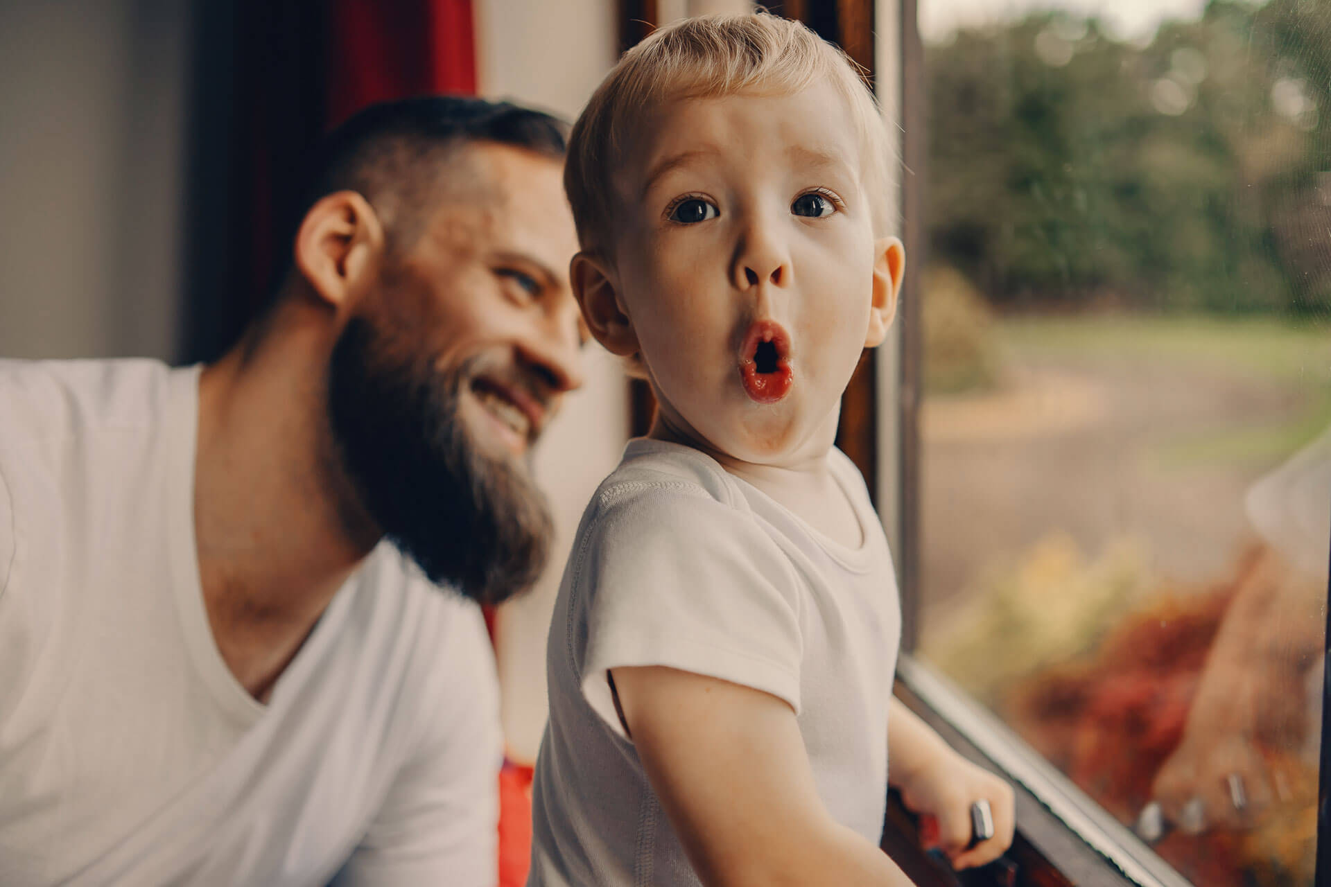 Young boy making a playful expression beside a window with his smiling father