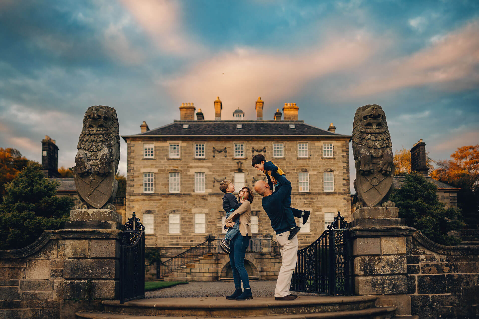 Parents holding their two children between stone lion statues outside Pollok House in Glasgow