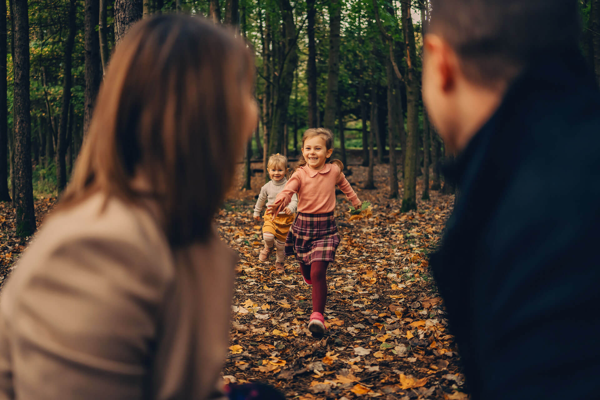Two smiling children running towards their parents through autumn woodland