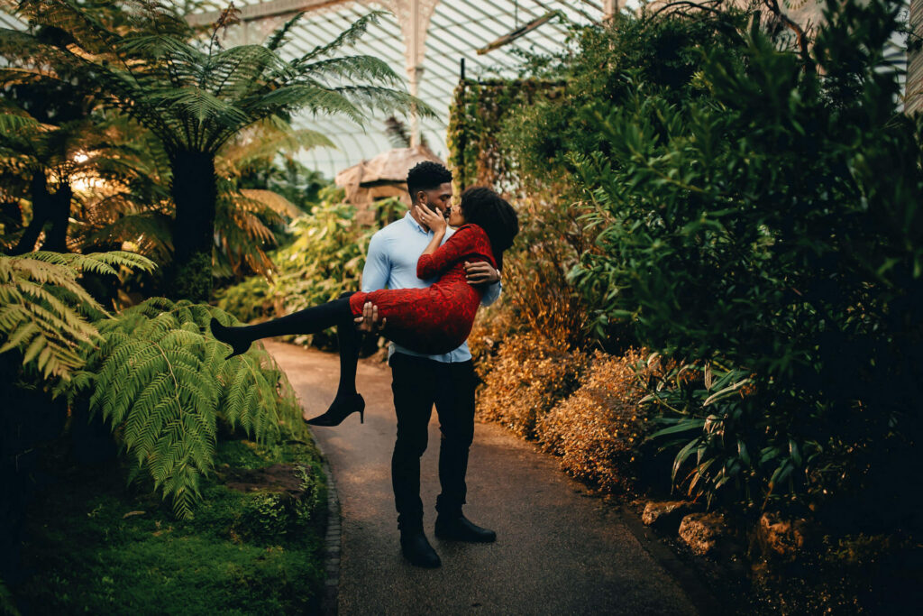 A man holding his fiancé in his arms  and kissing in the Botanic Garden in Glasgow