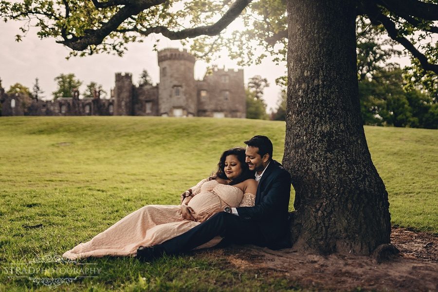 Pregnant woman laying on her husbands lap who is sitting at the bench near Balloch Castle