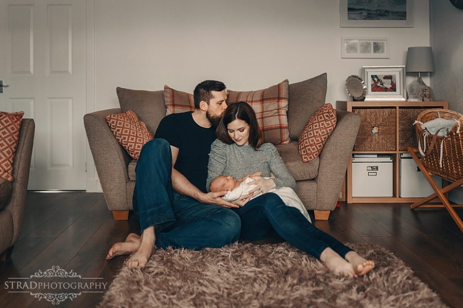 Man kisses his wife in the head and she is holding their newborn baby boy