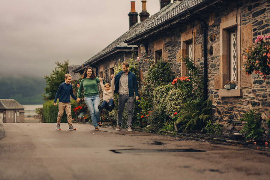 Family of four having fun walking and swinging kids in the air in Luss Town.