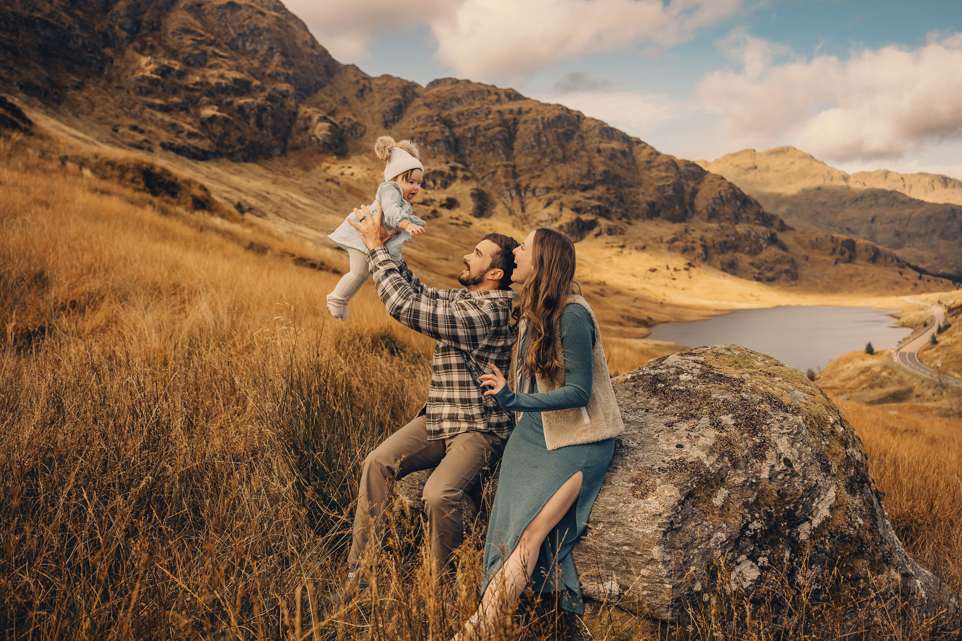 Father is holding his daughter in the air on a sunny day at the Rest and Be Thankful viewpoint in Scotland