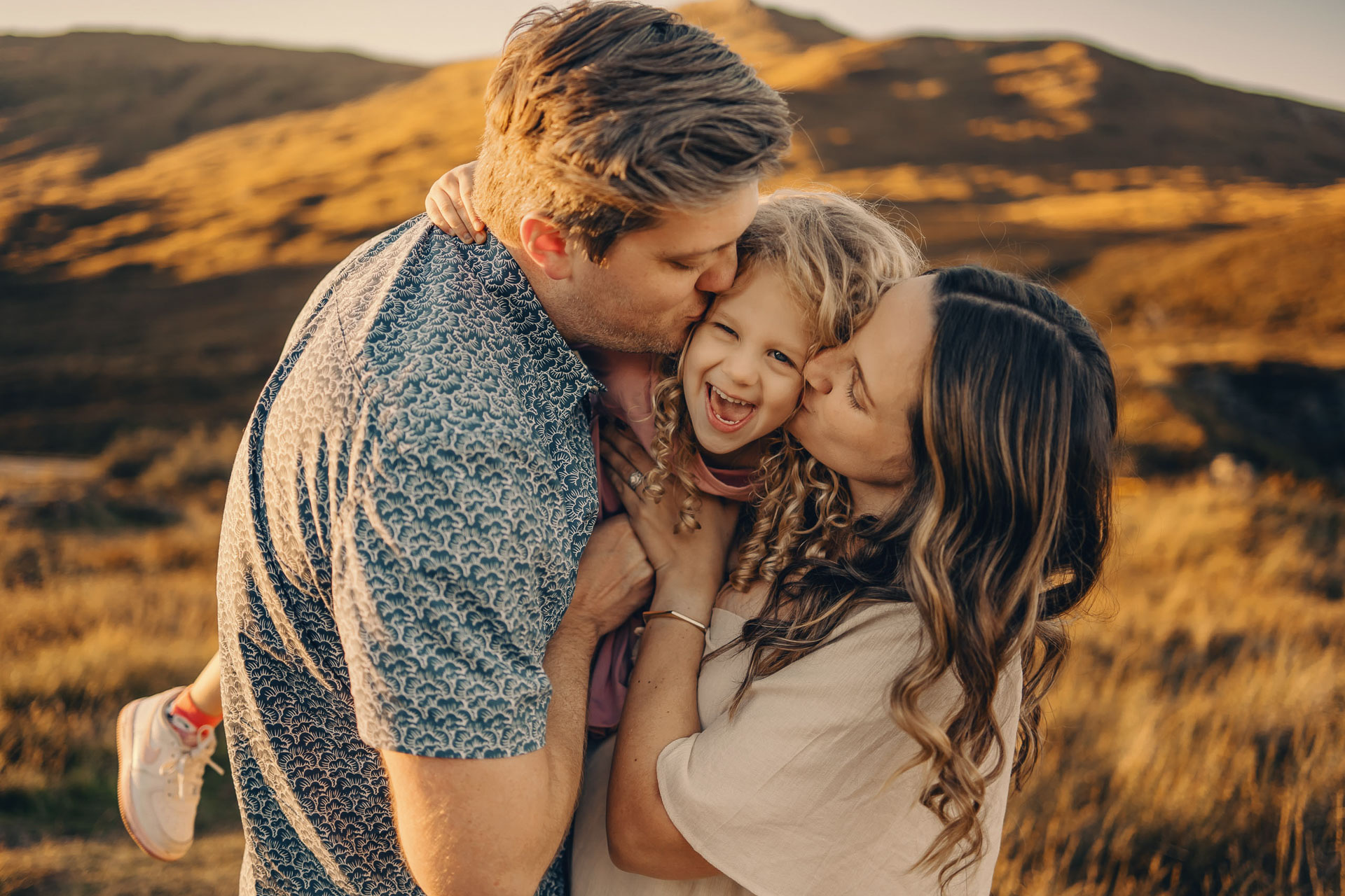 a mother and father kissing a child in Glencoe on a bright day