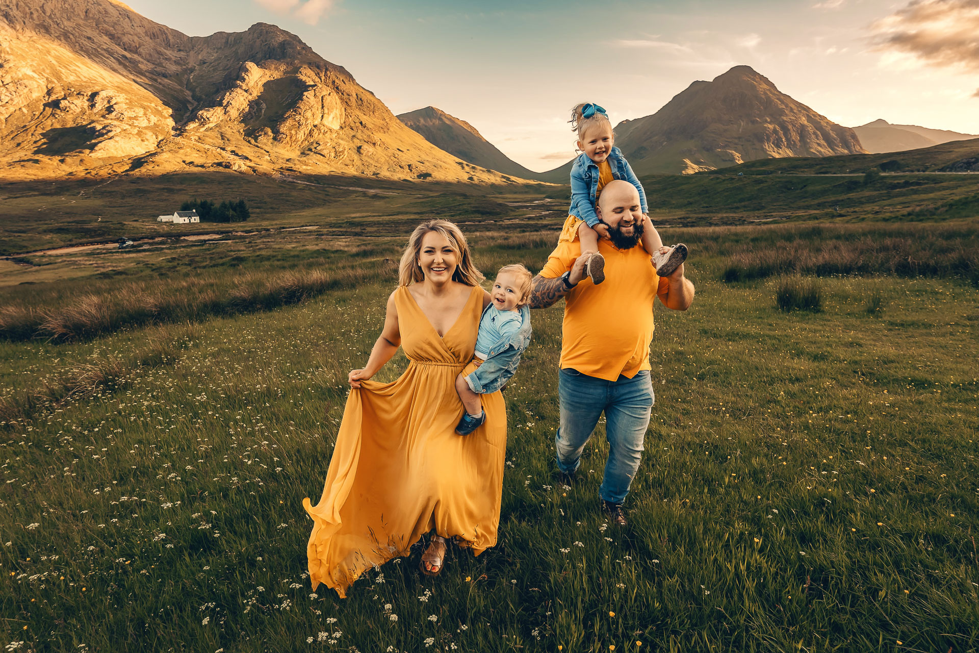 A mother in a yellow dress and father are running in a field with their two children in Glencoe