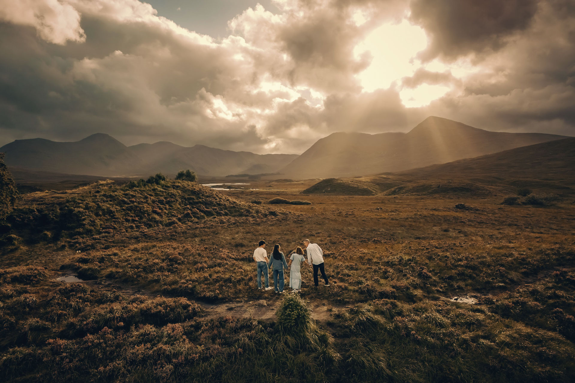 a family of four standing in a field with mountains and rays of light in the background