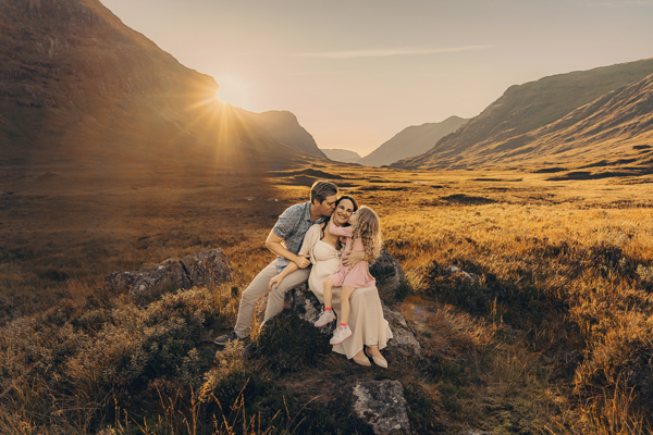 A family hugging on a rock in Glencoe with mountains and beautiful sunset in the background