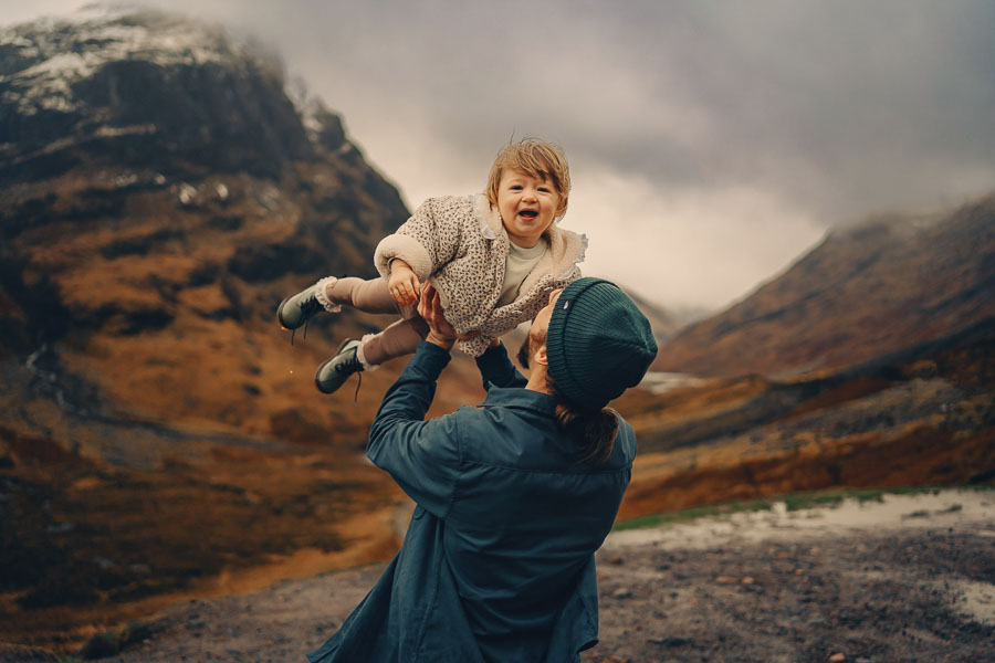 Parent lifting child in dramatic landscape.