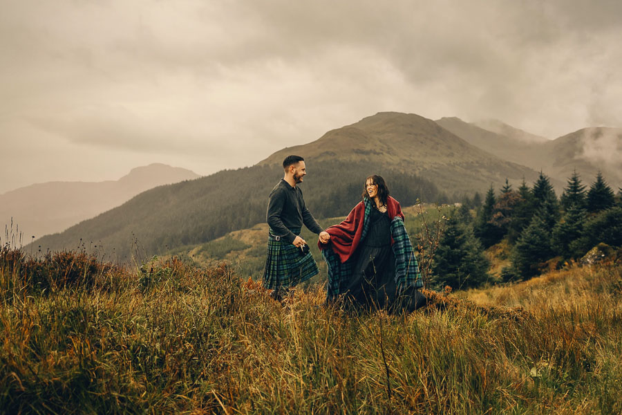 Couple in traditional Scottish attire outdoors.