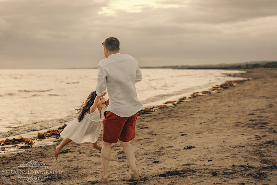 dad spinning daughter around at the beach