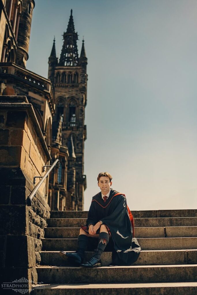 Graduate sitting on steps, university backdrop.