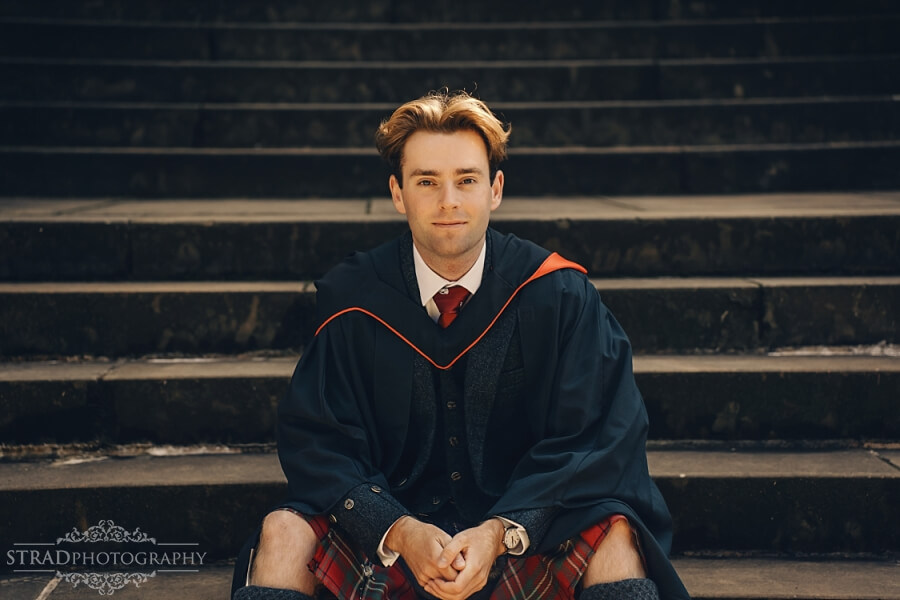 Graduate seated on steps in gown.
