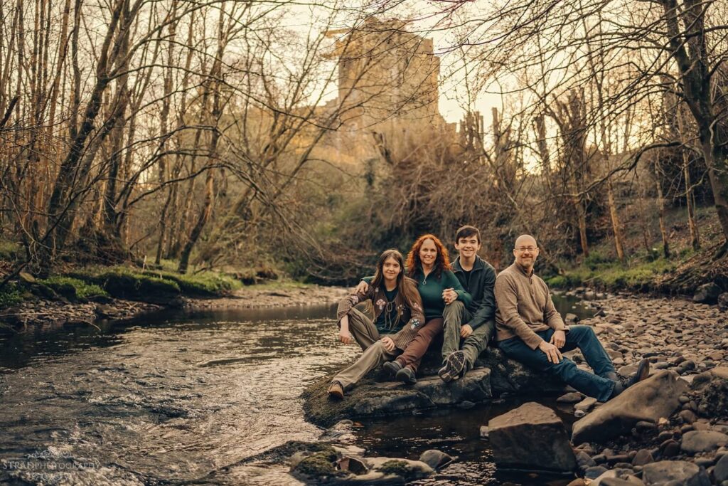 Family by a stream near trees.