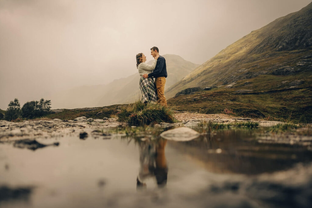 Couple embracing by a reflective pond.