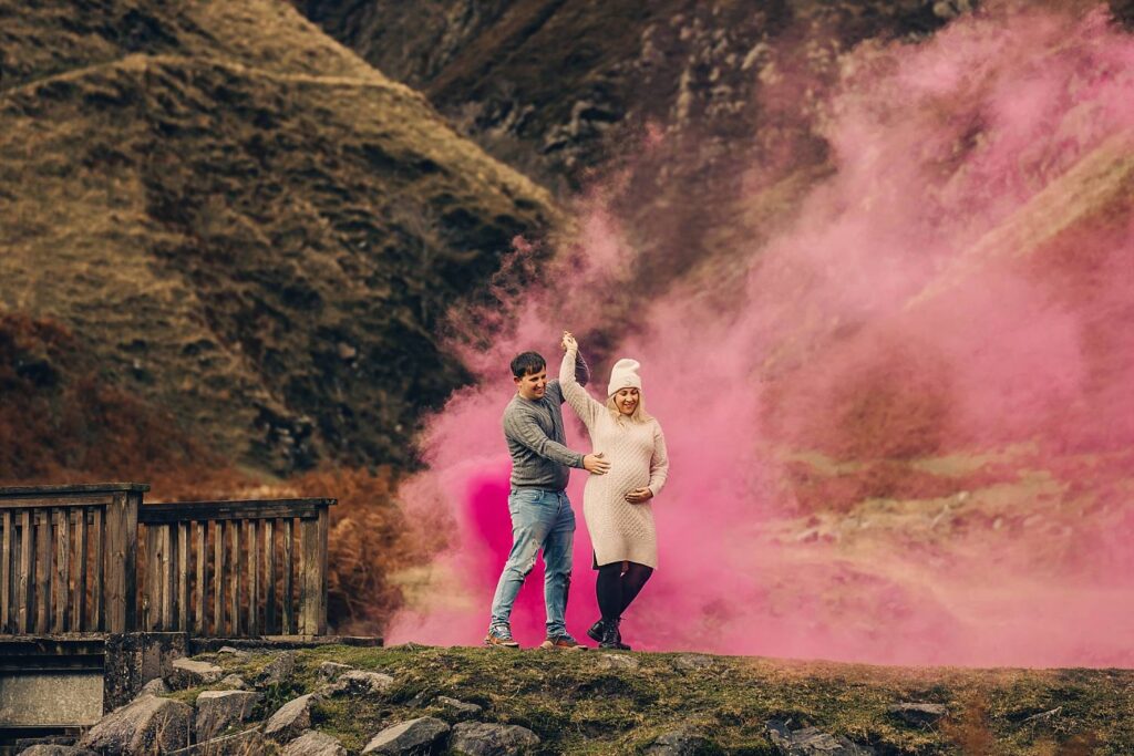 Pregnant couple using pink smoke bomb near waterfall